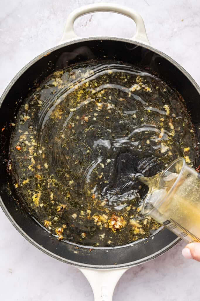 Pouring broth into skillet with garlic