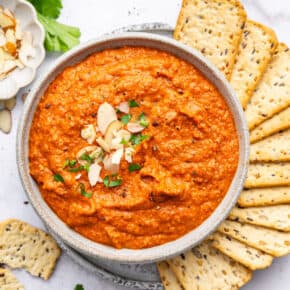 Overhead view of romesco sauce in bowl with crackers arranged on side
