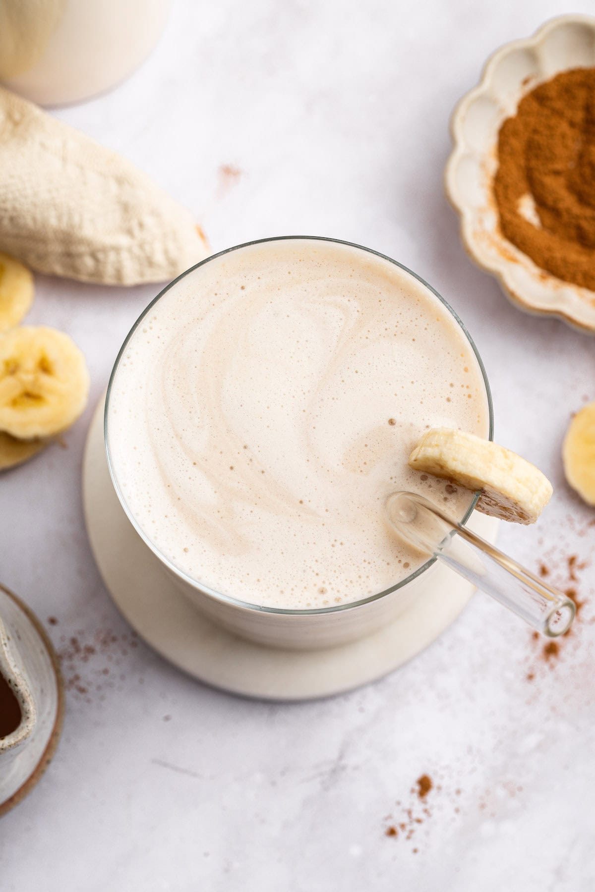 Overhead view of creamy banana milk in glass with straw and banana slice for garnish