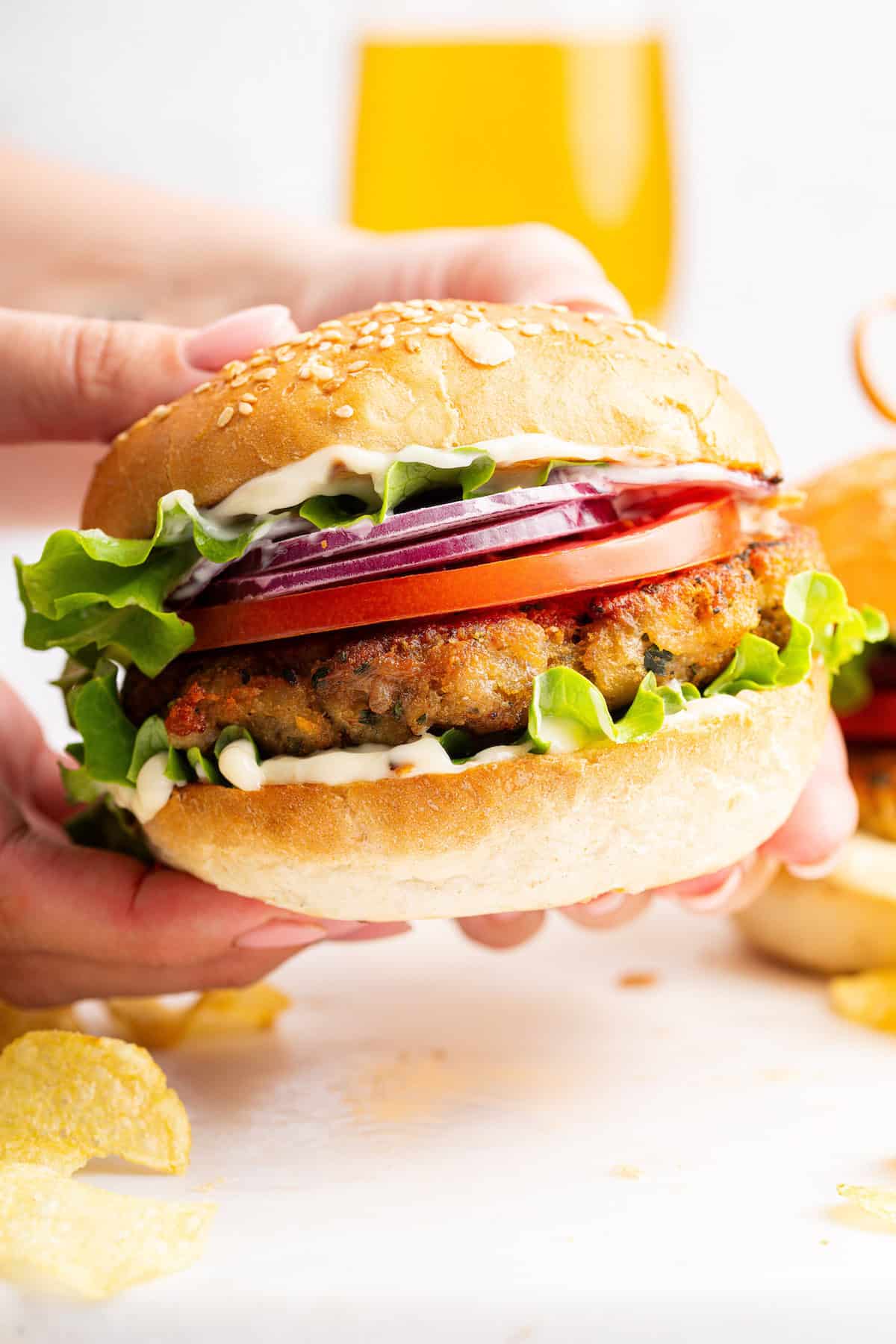 Hands holding chicken burger on sesame bun