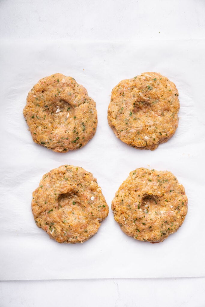 Overhead view of uncooked chicken burger patties with centers pressed in