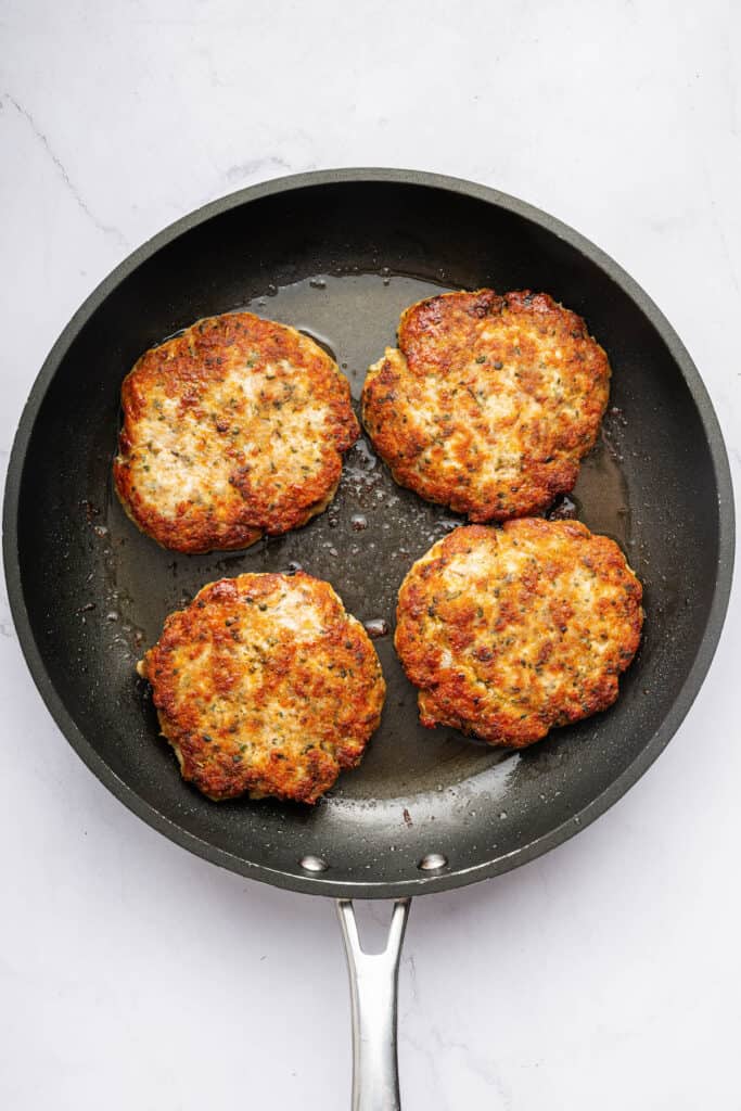 Overhead view of chicken burger patties in skillet