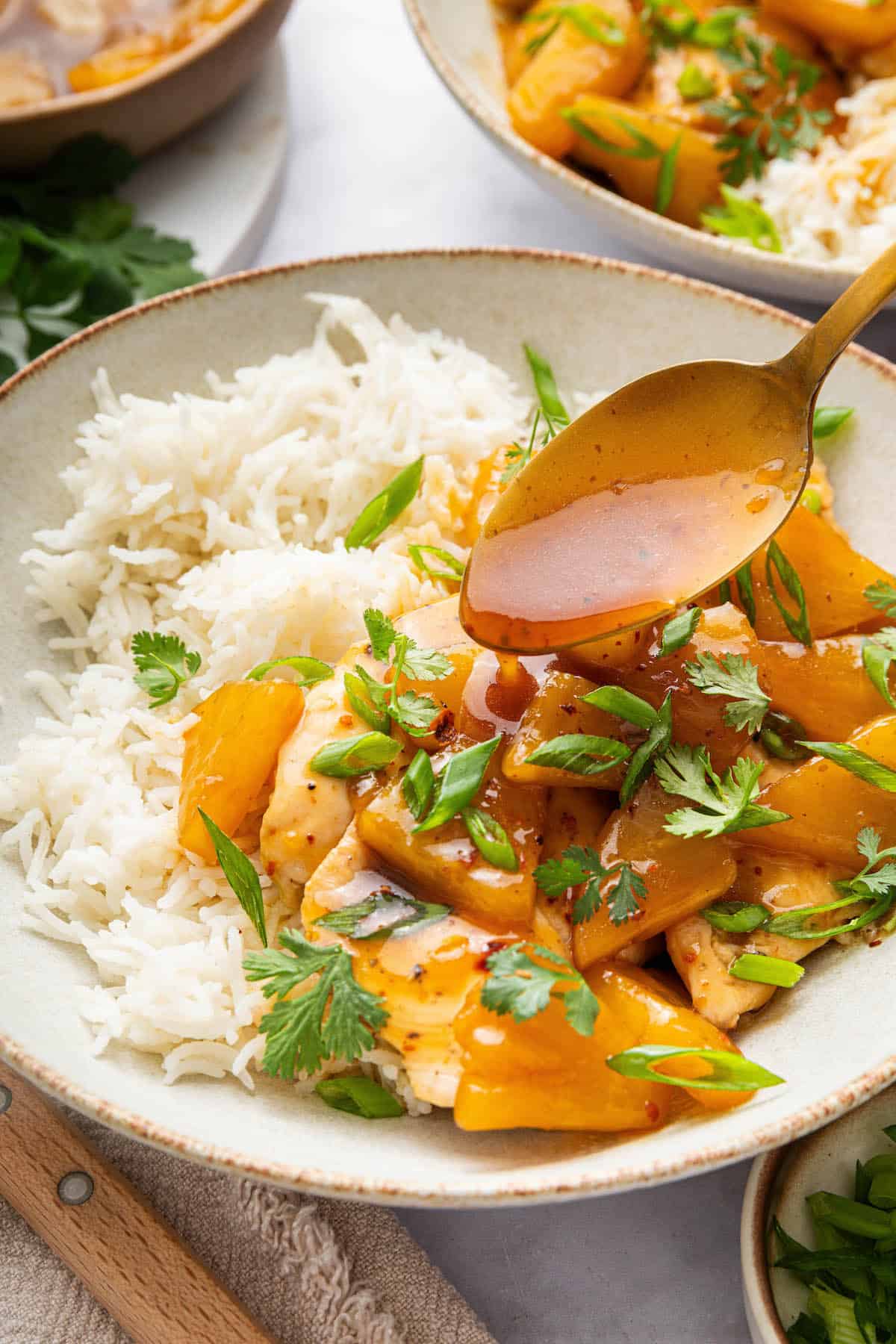 Spooning sauce over pineapple chicken in bowl with rice