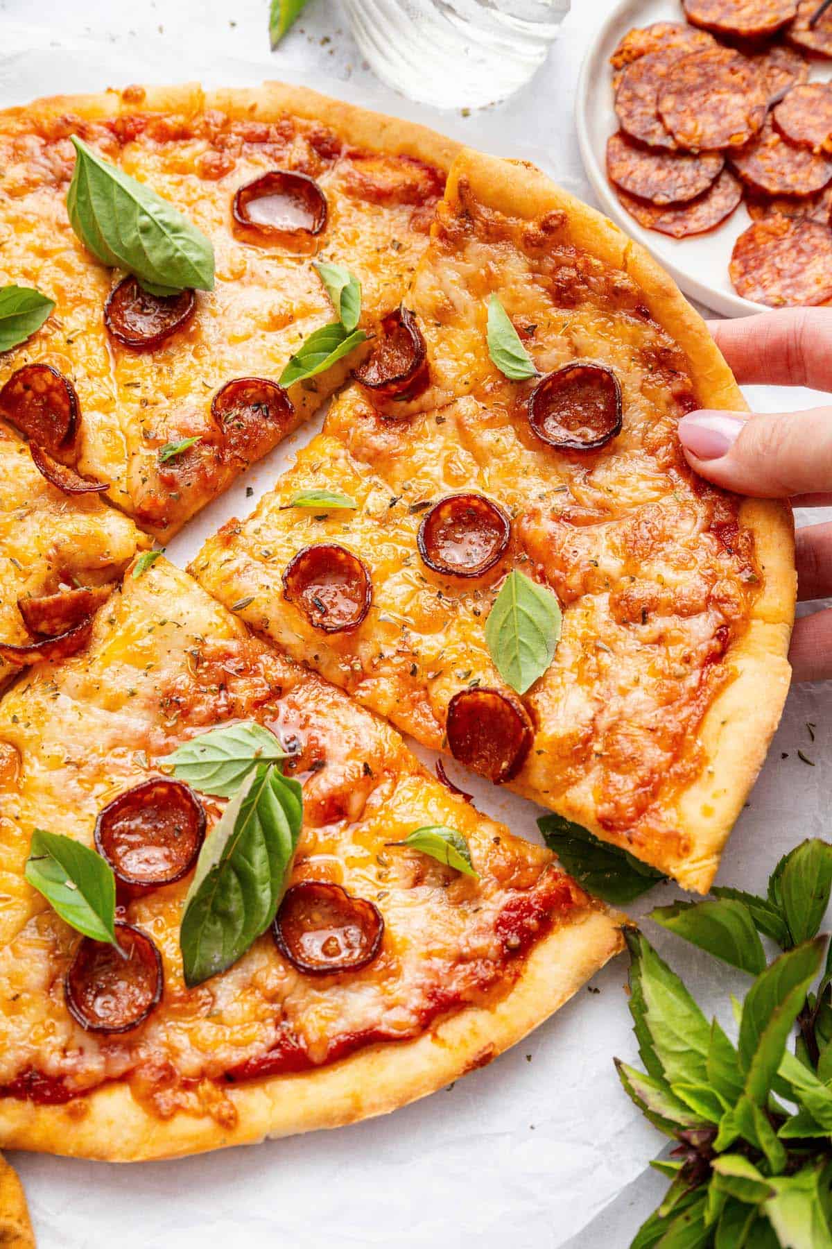 This Protein Pizza Crust is crisp and delicious, with Greek yogurt for a protein boost! Add your favorite toppings for a satisfying meal. Hand pulling slice of protein pizza crust topped with cheese and pepperoni