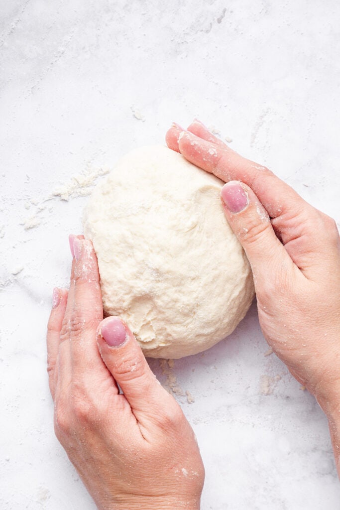 This Protein Pizza Crust is crisp and delicious, with Greek yogurt for a protein boost! Add your favorite toppings for a satisfying meal. Hands shaping protein pizza crust dough into ball