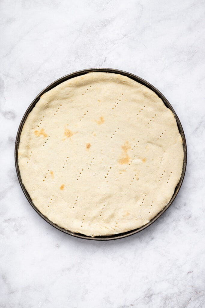 This Protein Pizza Crust is crisp and delicious, with Greek yogurt for a protein boost! Add your favorite toppings for a satisfying meal. Par-baked protein pizza crust pierced with fork