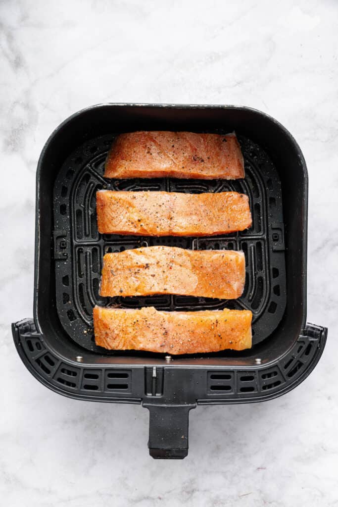 Yes, you can cook frozen salmon in the air fryer! It’s done in 25 minutes, ready for adding your favorite sauces, garnishes, and sides. Overhead view of frozen salmon fillets in air fryer basket