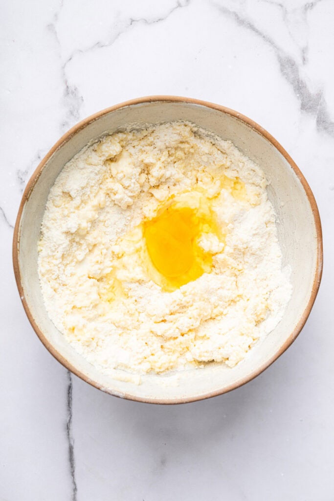 This blueberry peach cobbler recipe pairs two summer favorites in a jammy filling that’s baked with a buttery, flaky topping. So easy! Overhead view of egg cracked into bowl of cobbler topping