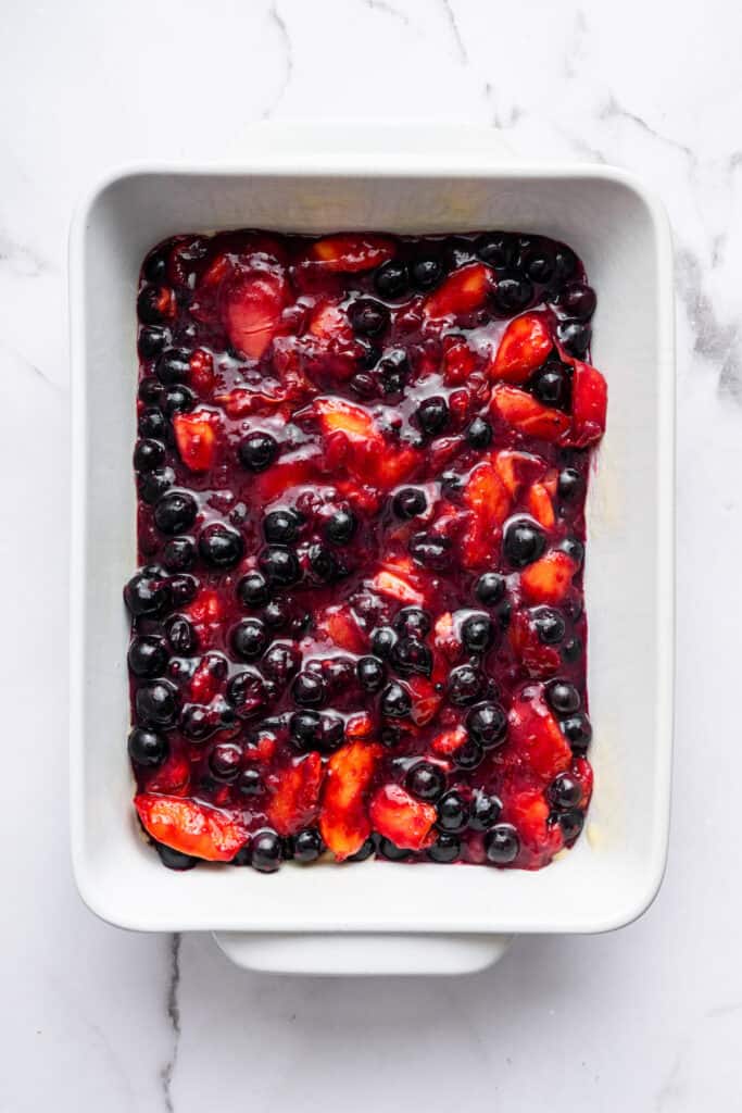 This blueberry peach cobbler recipe pairs two summer favorites in a jammy filling that’s baked with a buttery, flaky topping. So easy! Overhead view of blueberry and peach filling in baking dish