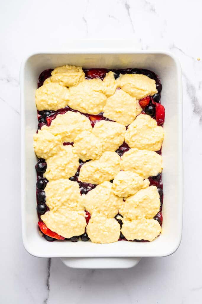 This blueberry peach cobbler recipe pairs two summer favorites in a jammy filling that’s baked with a buttery, flaky topping. So easy! Overhead view of blueberry peach cobbler in baking dish before baking