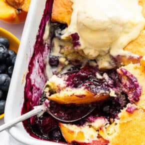 Spoon scooping blueberry peach cobbler from baking dish