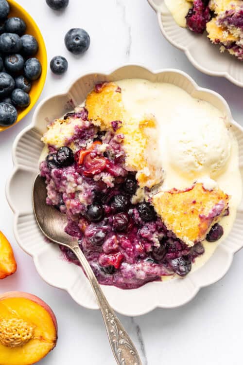 Overhead view of blueberry peach cobbler in bowl with vanilla ice cream