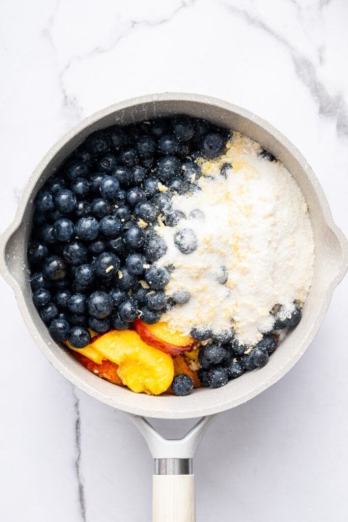 This blueberry peach cobbler recipe pairs two summer favorites in a jammy filling that’s baked with a buttery, flaky topping. So easy! Overhead view of blueberries, peaches, and flour mixture in saucepan