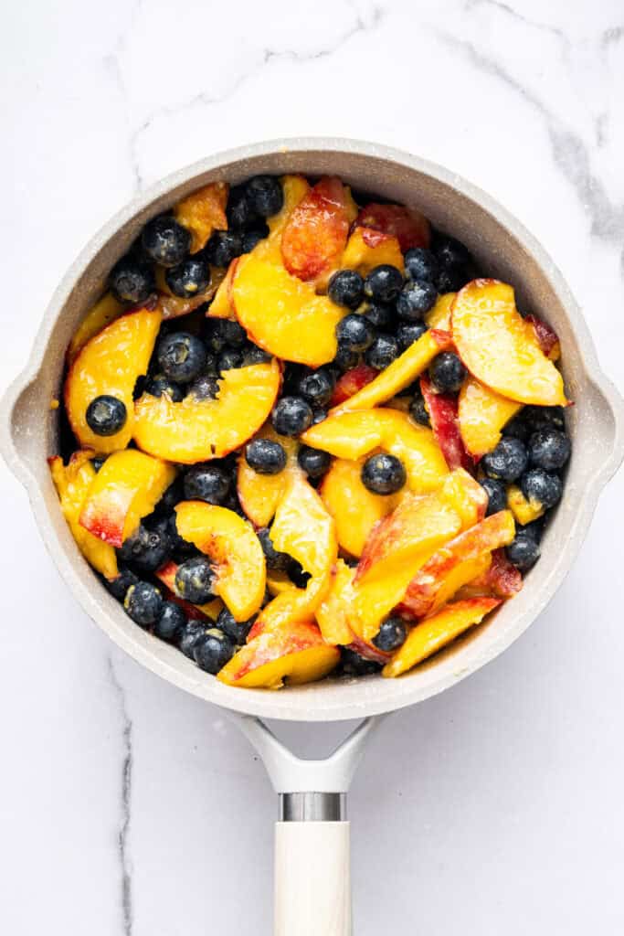 This blueberry peach cobbler recipe pairs two summer favorites in a jammy filling that’s baked with a buttery, flaky topping. So easy! Overhead view of fresh peaches and blueberries added to saucepan