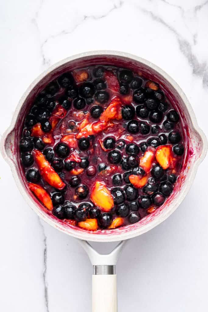 This blueberry peach cobbler recipe pairs two summer favorites in a jammy filling that’s baked with a buttery, flaky topping. So easy! Overhead view of blueberries and peaches cooked in saucepan