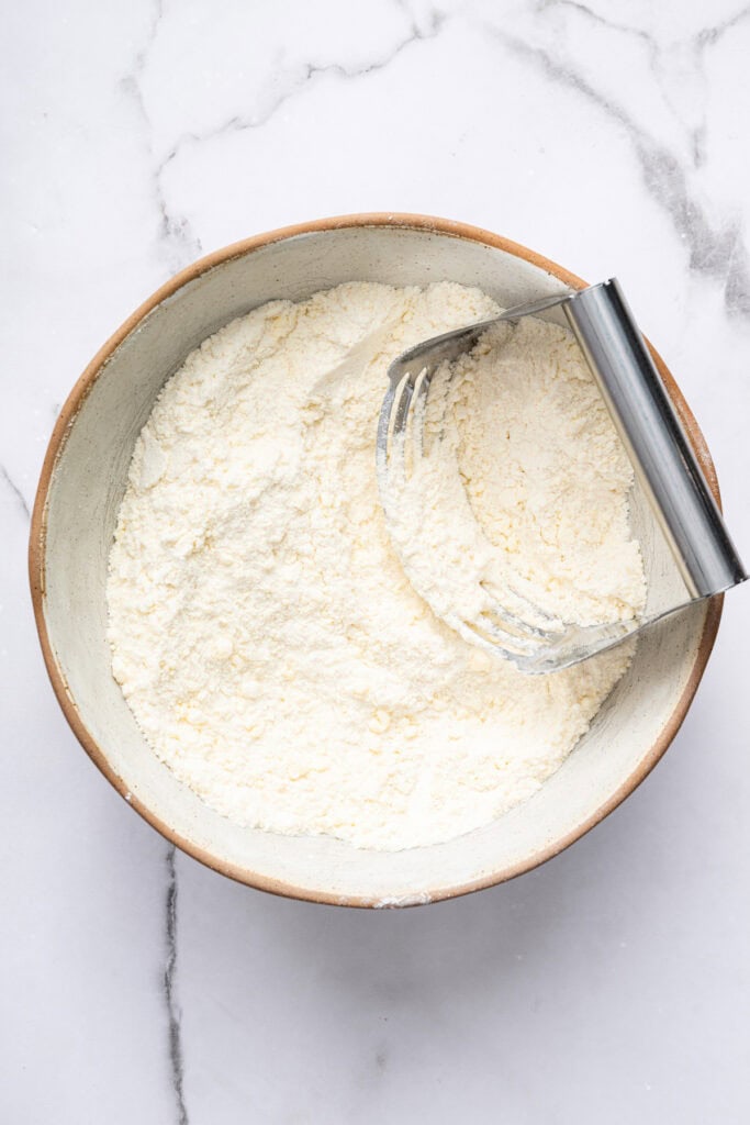 This blueberry peach cobbler recipe pairs two summer favorites in a jammy filling that’s baked with a buttery, flaky topping. So easy! Pastry blender in bowl of cobbler topping