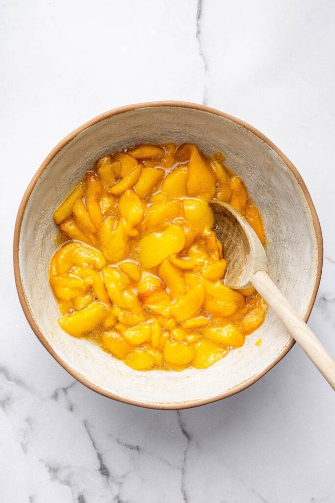 Overhead view of peaches and sugar in bowl with wooden spoon