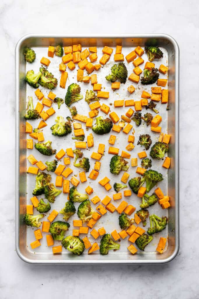 With flaky salmon, grains and veggies, this Salmon Power Bowl recipe is an easy meal prep option that will fuel you through your day! Overhead view of roasted sweet potatoes and broccoli on sheet pan