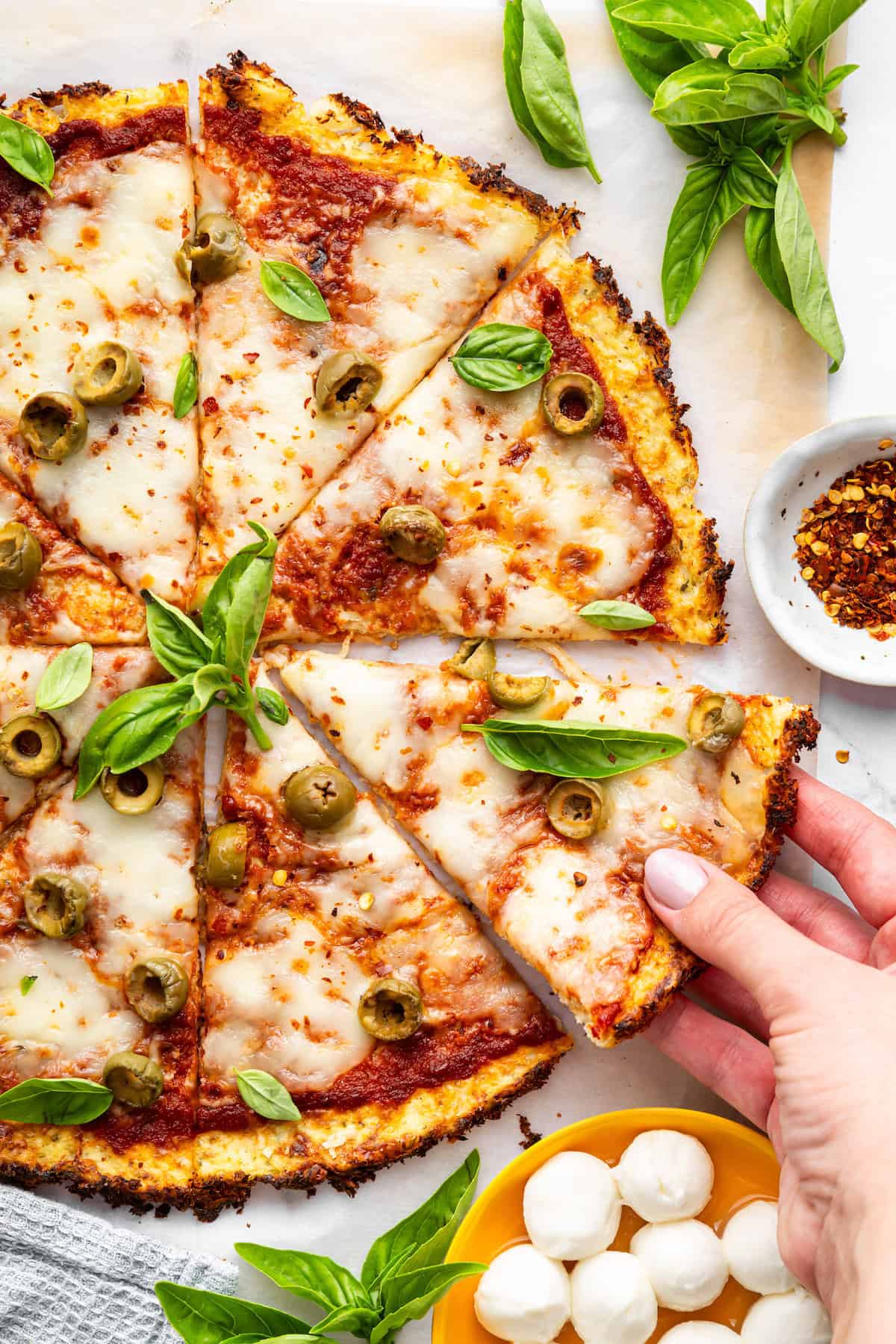 Hand holding slice of cauliflower crust pizza
