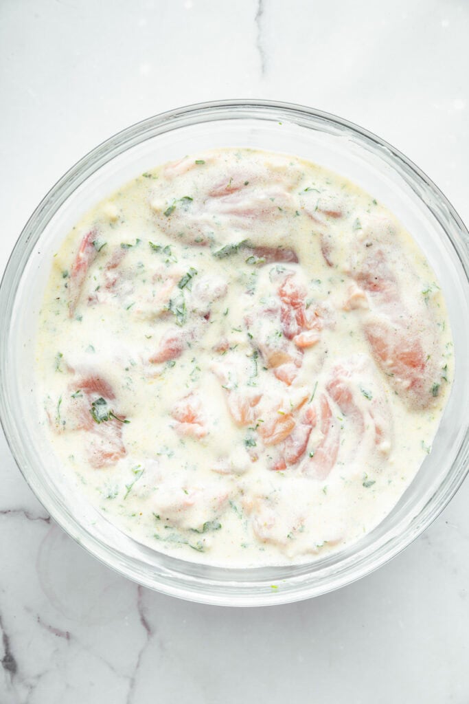 Overhead view of chicken in bowl of Greek yogurt marinade