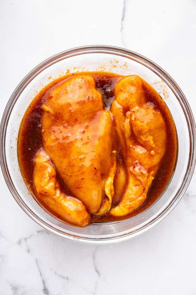 Chicken breasts in bowl with harissa honey marinade.