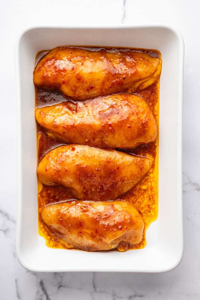 Harissa honey chicken in baking dish with sauce before baking.