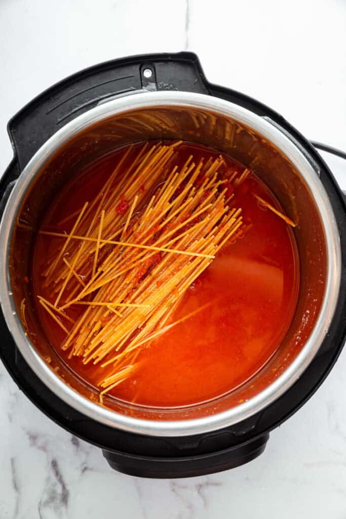 This two-ingredient Instant Pot Spaghetti cooks the pasta in the sauce, and it does it in a pressure cooker so it takes just 20 minutes! Overhead view of dry spaghetti in Instant Pot with sauce and water
