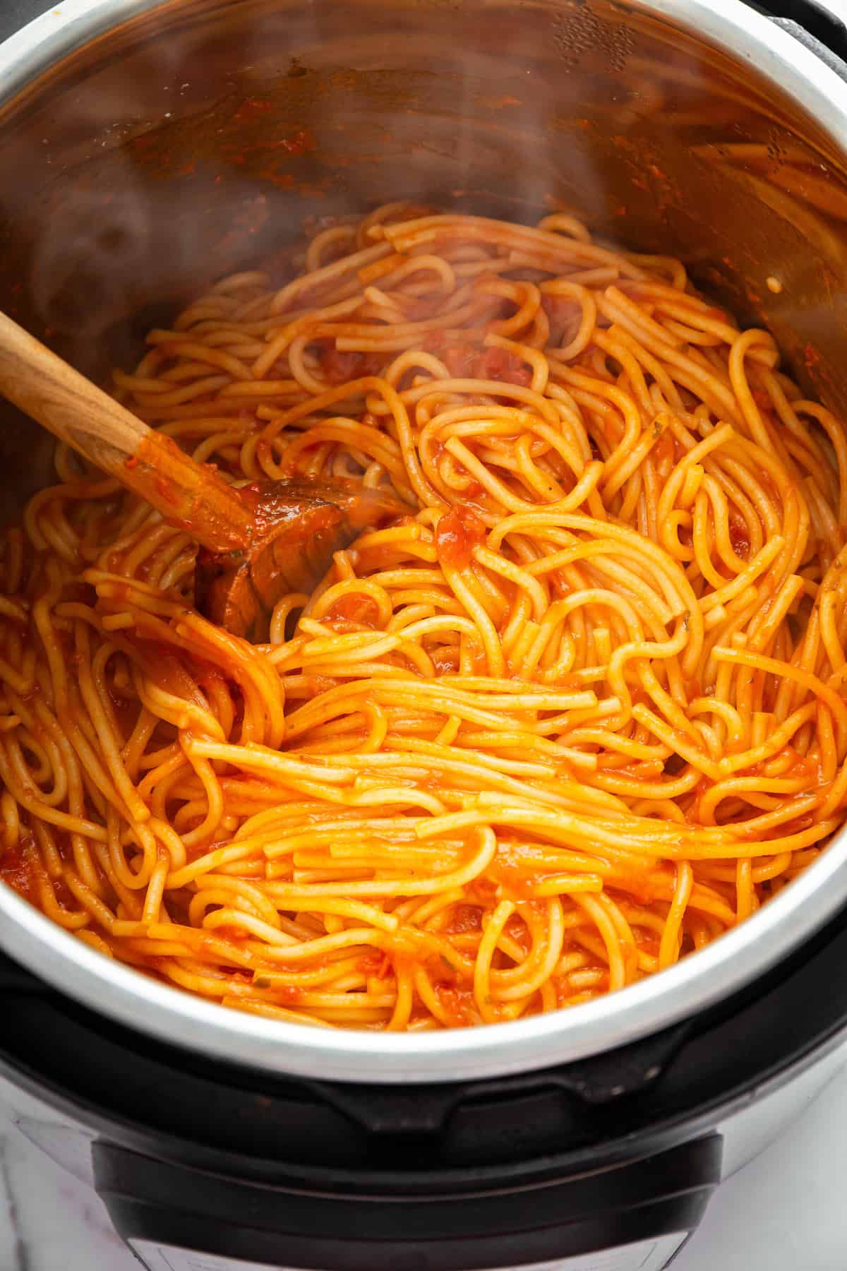This two-ingredient Instant Pot Spaghetti cooks the pasta in the sauce, and it does it in a pressure cooker so it takes just 20 minutes! Overhead view of wooden spoon stirring spaghetti in Instant Pot