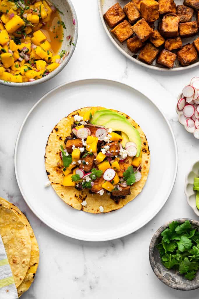 With black beans, crispy tofu and a sweet, tangy mango-peach salsa, these Air Fryer Tofu Tacos are the tastiest meatless dinner ever! Overhead view of air fryer tofu taco on plate with cotija