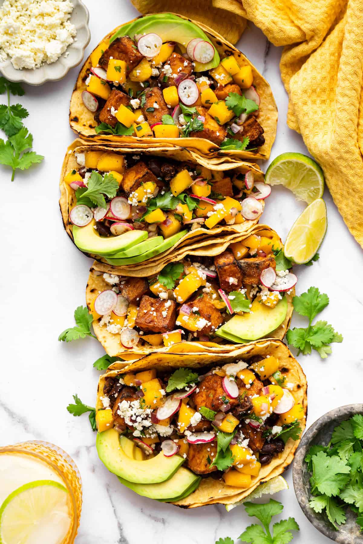 With black beans, crispy tofu and a sweet, tangy mango-peach salsa, these Air Fryer Tofu Tacos are the tastiest meatless dinner ever! Overhead view of 4 air fryer tofu tacos lined up on counter