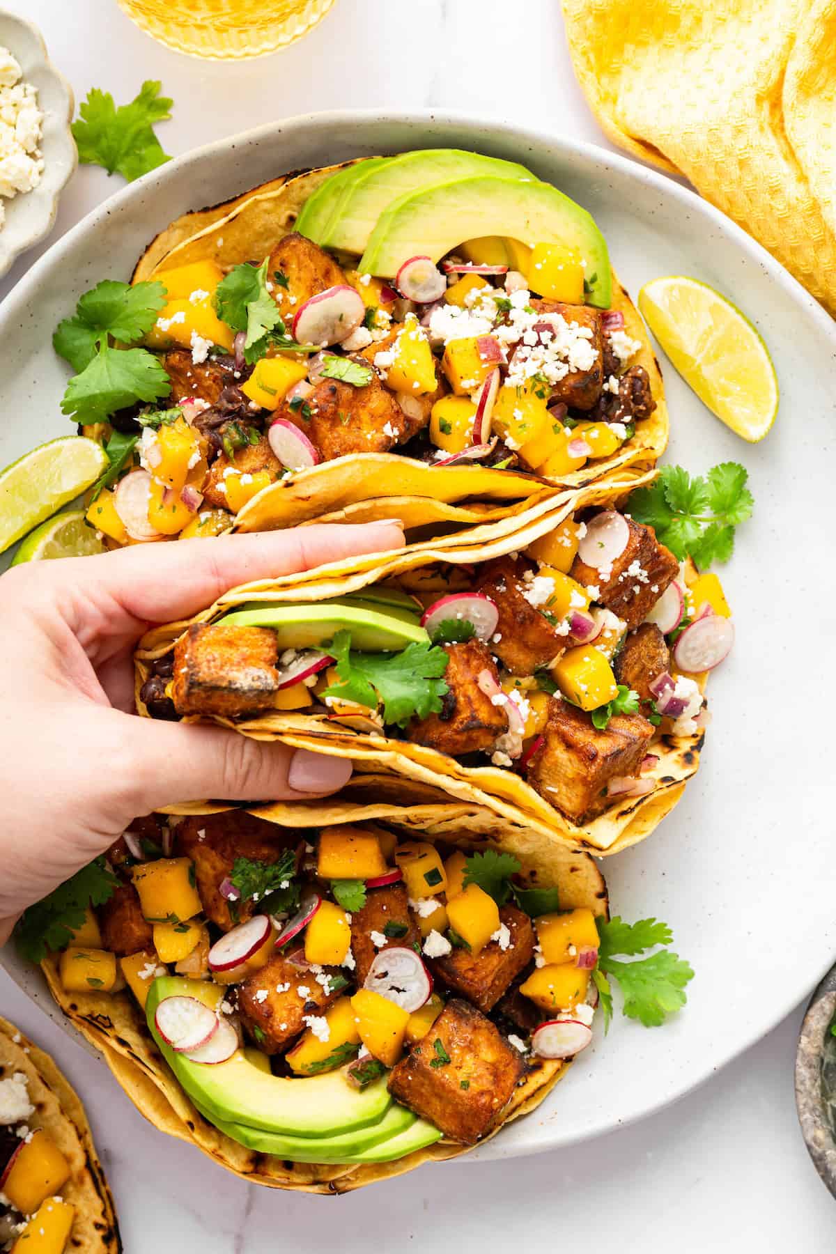 With black beans, crispy tofu and a sweet, tangy mango-peach salsa, these Air Fryer Tofu Tacos are the tastiest meatless dinner ever! Hand picking up air fryer tofu taco from plate