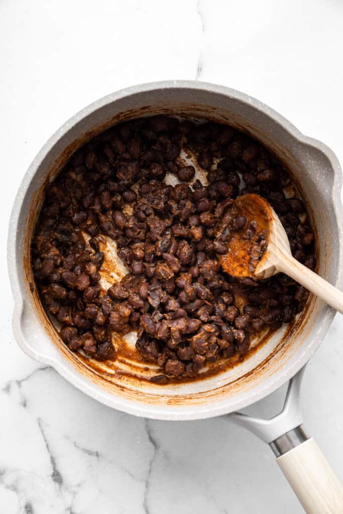 With black beans, crispy tofu and a sweet, tangy mango-peach salsa, these Air Fryer Tofu Tacos are the tastiest meatless dinner ever! Overhead view of black beans in pan with wooden spoon