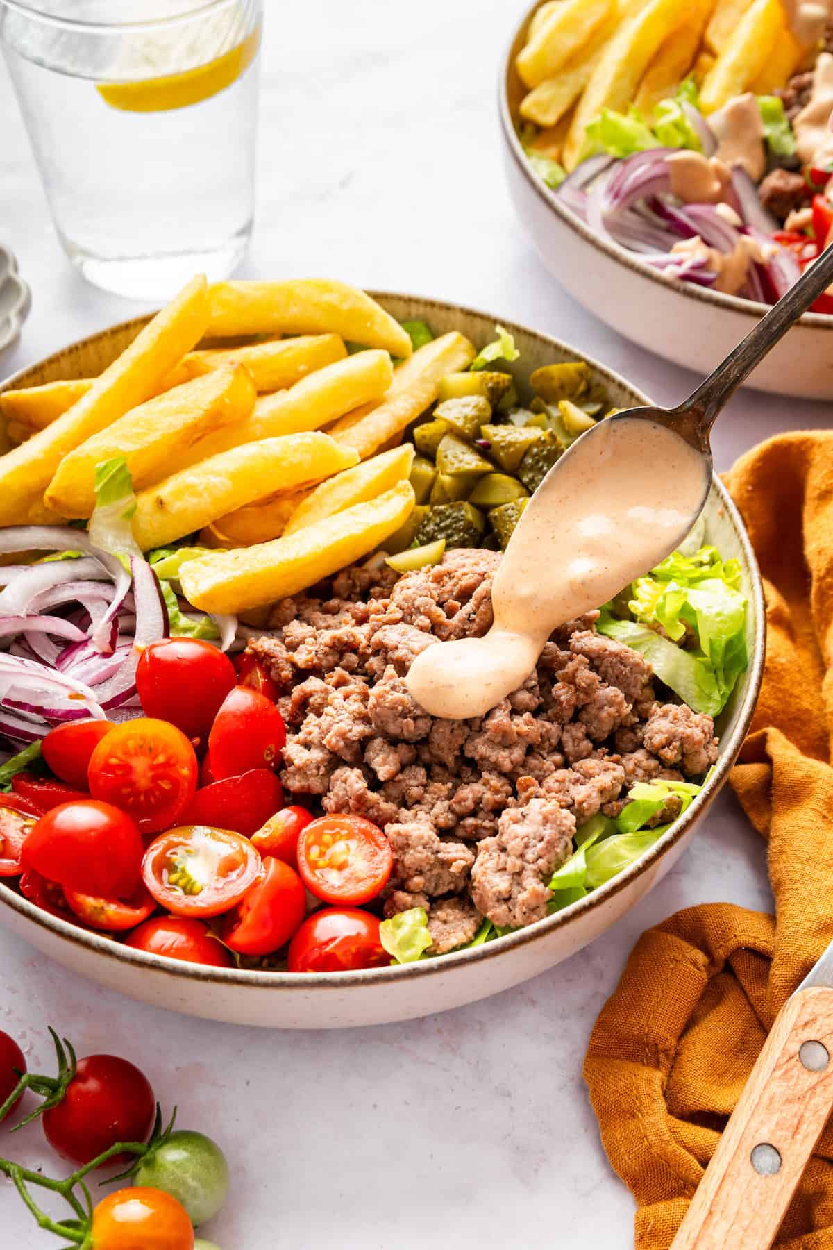 This Burger Bowl recipe gives you your burger fix, without the bun! It’s a fun protein-packed meal with crispy fries and your fave toppings. Spoon drizzling special sauce onto burger bowl.
