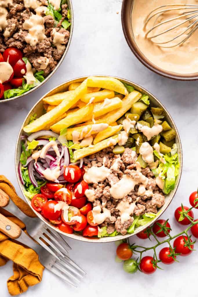 This Burger Bowl recipe gives you your burger fix, without the bun! It’s a fun protein-packed meal with crispy fries and your fave toppings. Two burger bowls with bowl of special sauce.