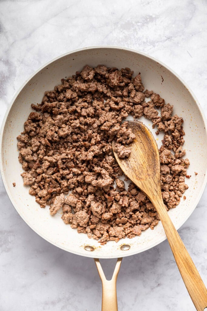 This Burger Bowl recipe gives you your burger fix, without the bun! It’s a fun protein-packed meal with crispy fries and your fave toppings. Ground beef browned in skillet with wooden spoon.