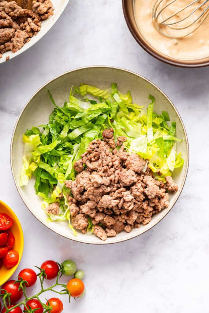 This Burger Bowl recipe gives you your burger fix, without the bun! It’s a fun protein-packed meal with crispy fries and your fave toppings. Lettuce and ground beef in bowl.