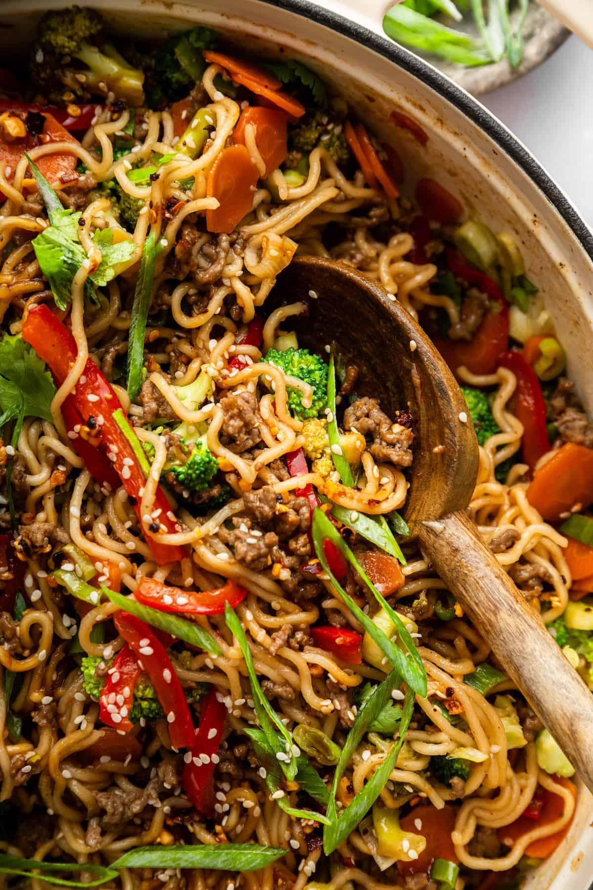 Springy ramen noodles are combined with ground beef and veggies to make this super easy one pan Beef Ramen recipe. Done in 25 minutes! Wooden spoon in pan of beef ramen.