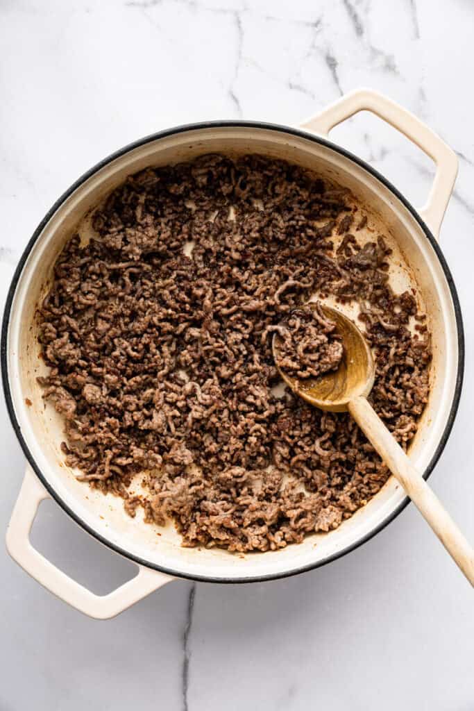 Springy ramen noodles are combined with ground beef and veggies to make this super easy one pan Beef Ramen recipe. Done in 25 minutes! Ground beef in skillet with wooden spoon.