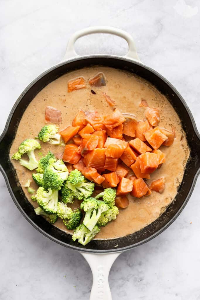 This flavorful Salmon Curry is a 30-minute dinner with creamy coconut sauce, broccoli and spinach. Serve over rice for a filling meal! Salmon and broccoli added to coconut curry sauce in skillet.