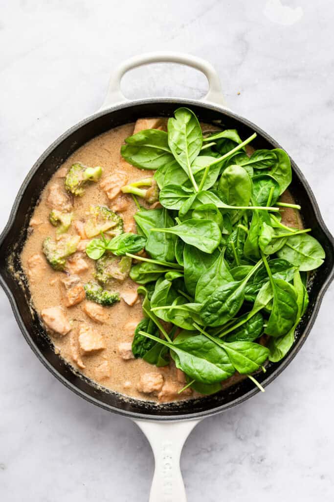 This flavorful Salmon Curry is a 30-minute dinner with creamy coconut sauce, broccoli and spinach. Serve over rice for a filling meal! Spinach added to pan of salmon curry.