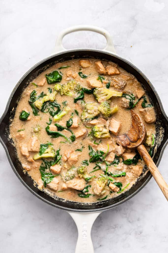 This flavorful Salmon Curry is a 30-minute dinner with creamy coconut sauce, broccoli and spinach. Serve over rice for a filling meal! Stirring salmon curry in skillet.