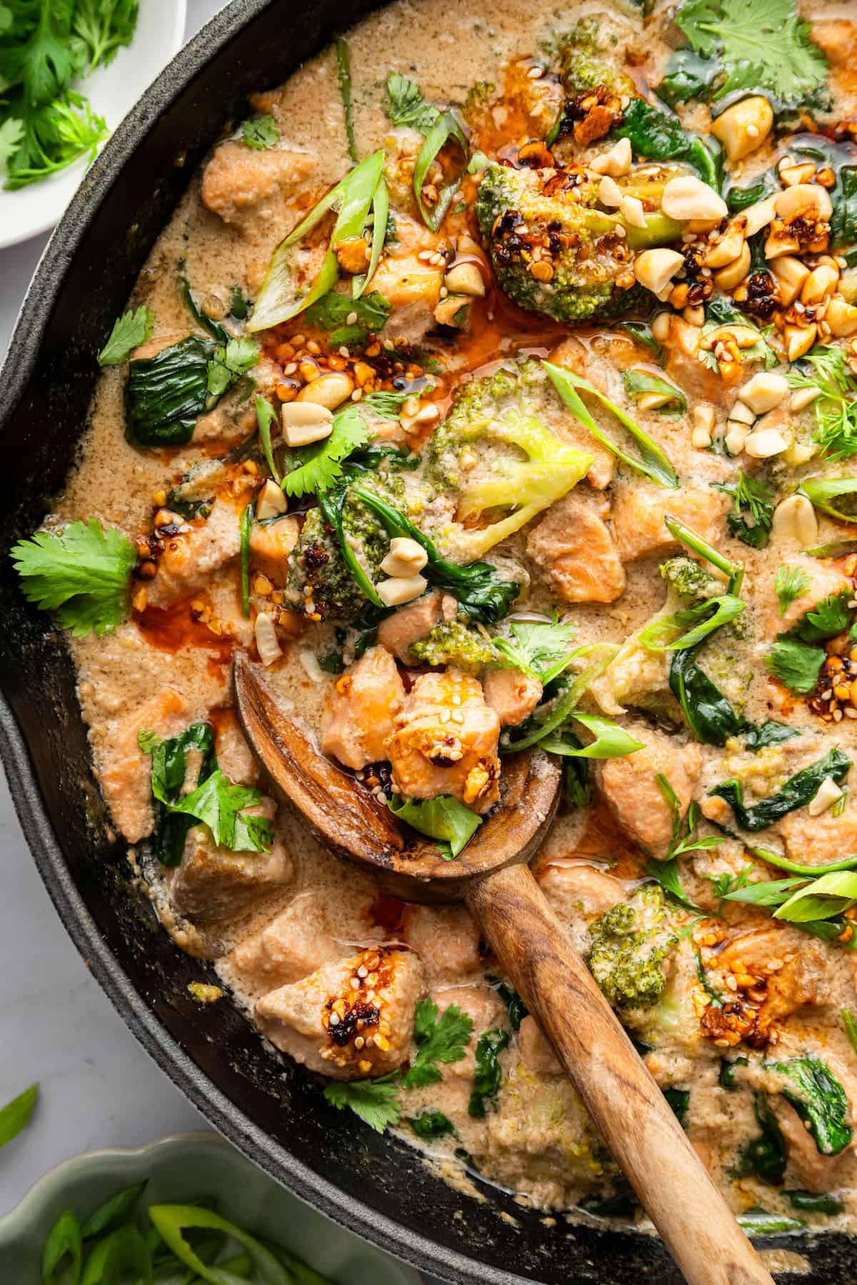 This flavorful Salmon Curry is a 30-minute dinner with creamy coconut sauce, broccoli and spinach. Serve over rice for a filling meal! Salmon curry with spinach and broccoli in skillet with wooden spoon.