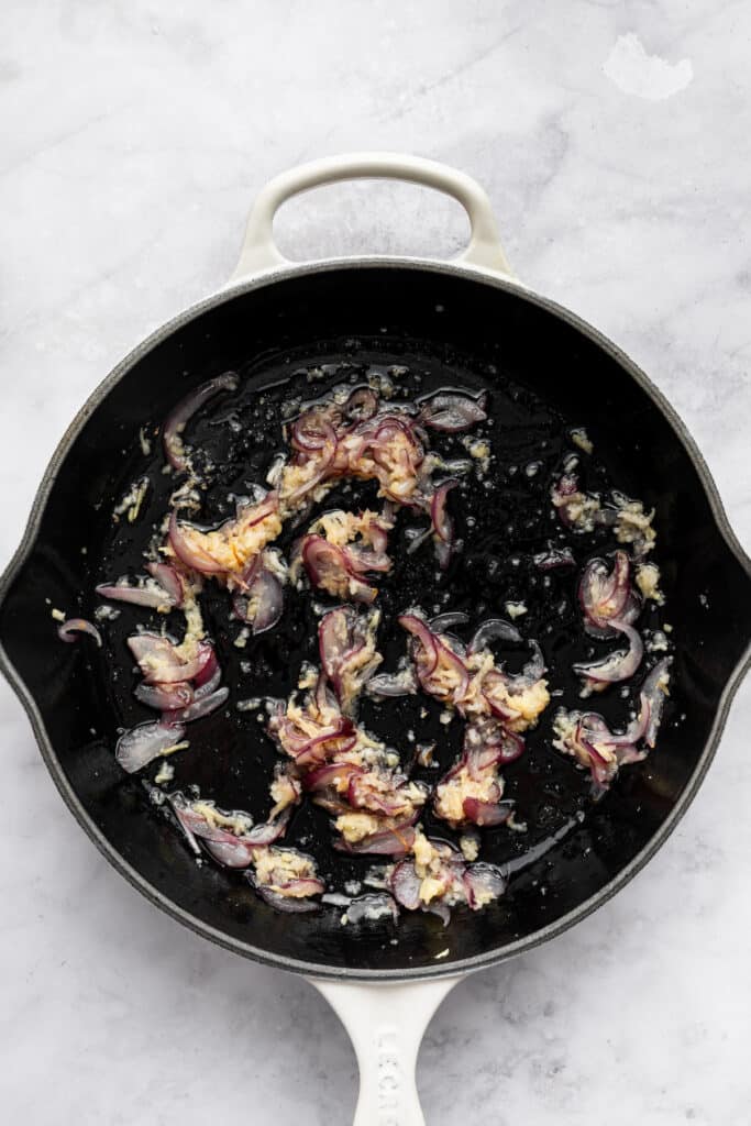 This flavorful Salmon Curry is a 30-minute dinner with creamy coconut sauce, broccoli and spinach. Serve over rice for a filling meal! Red onion, garlic, and ginger cooking in coconut oil.