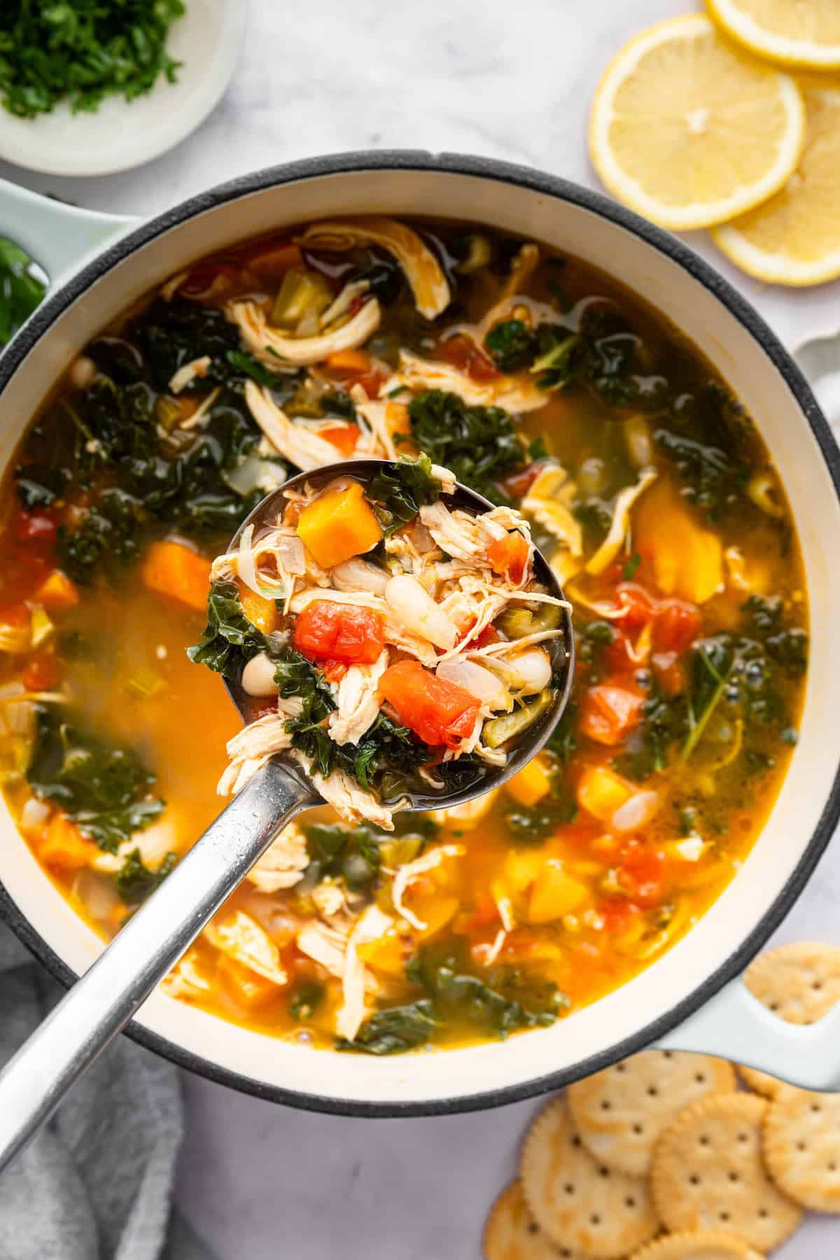 Ladle of chicken vegetable soup held over pot.