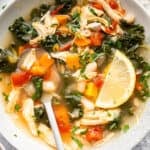 Bowl of chicken vegetable soup with spoon and lemon slice.