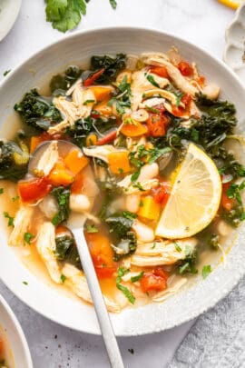 Bowl of chicken vegetable soup with spoon and lemon slice.