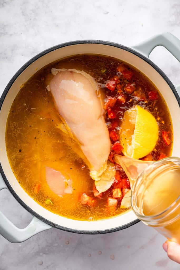Pouring vegetable broth into pot for chicken vegetable soup.