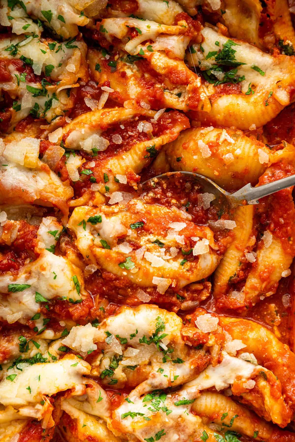 Spoon digging into dish of stuffed shells.