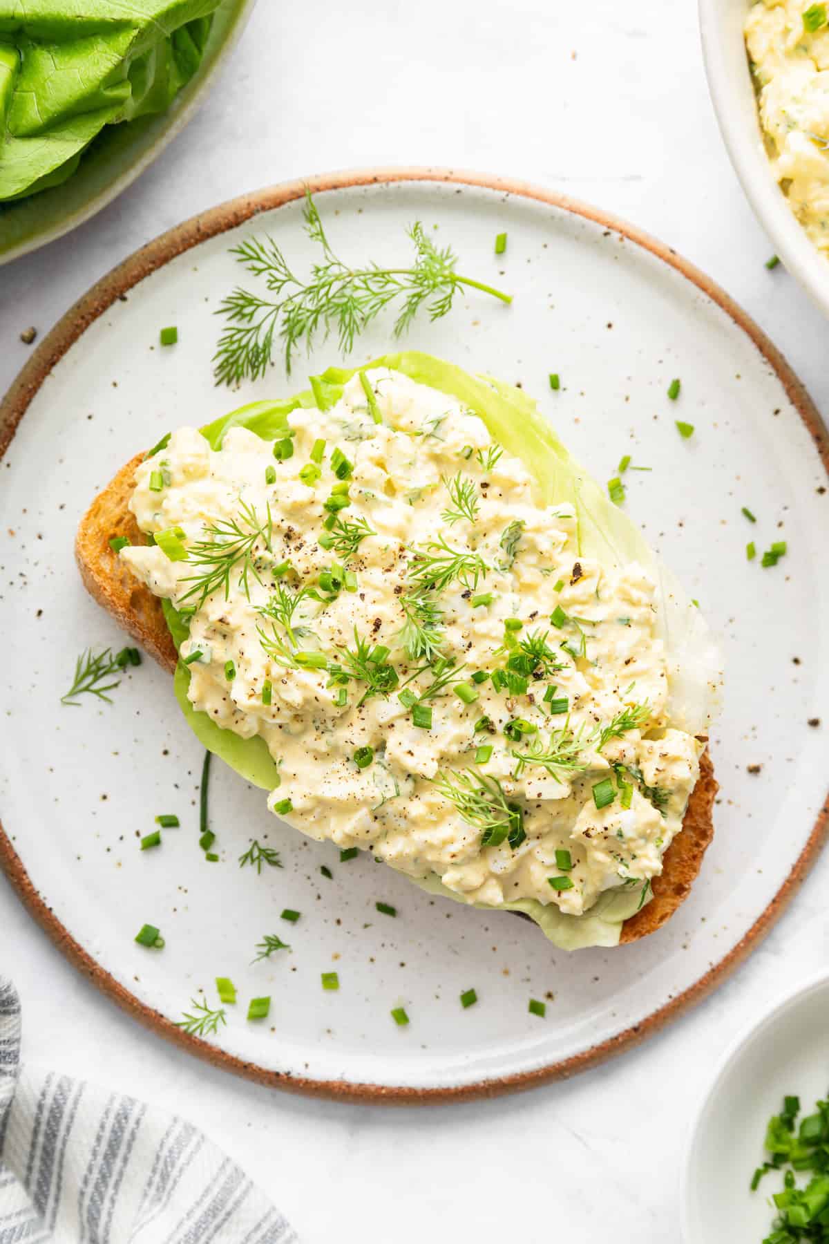 Egg salad on slice of toast with fresh herbs.