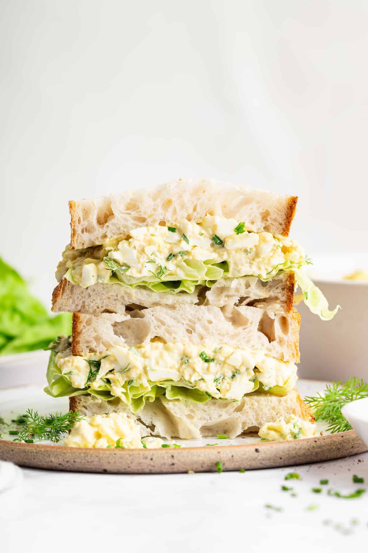 Two halves of an egg salad sandwich stacked on plate.